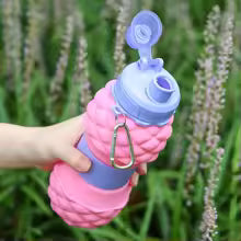 Pink foldable silicone bottle 700ml with blue cap and carabiner clip held outdoors