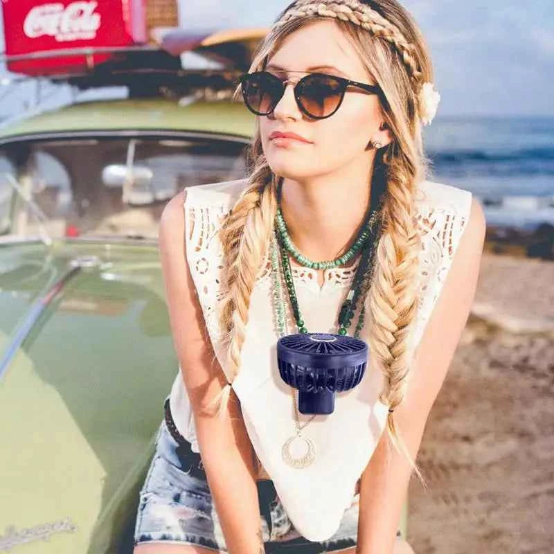 Stylish woman with sunglasses and braids using a foldable USB table fan on a beach outing