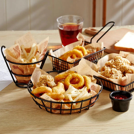 Black metal french fries basket set with crispy fries, onion rings, fried chicken, and dipping sauce on a wooden table