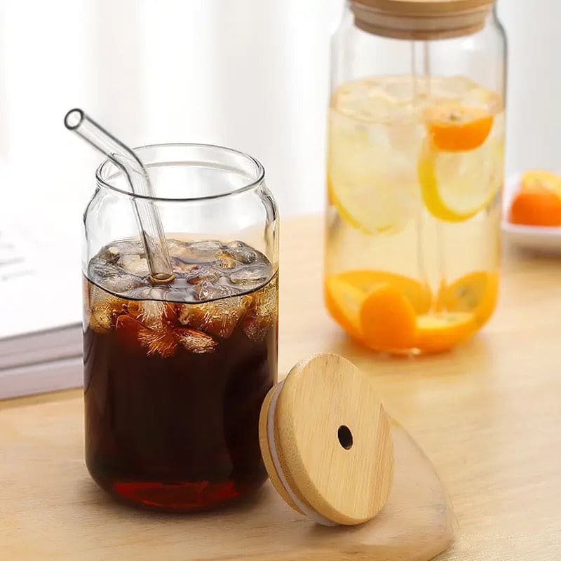 Clear bamboo lid iced coffee mug with ice cubes and glass straw on wooden surface