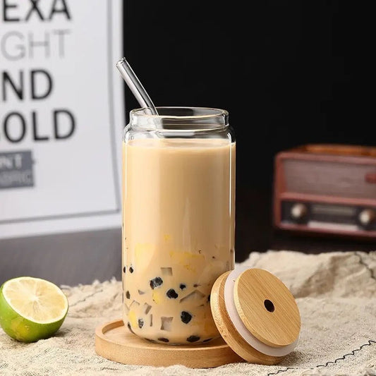 Glass cup with a bamboo lid iced coffee mug filled with iced coffee and a metal straw on a wooden coaster