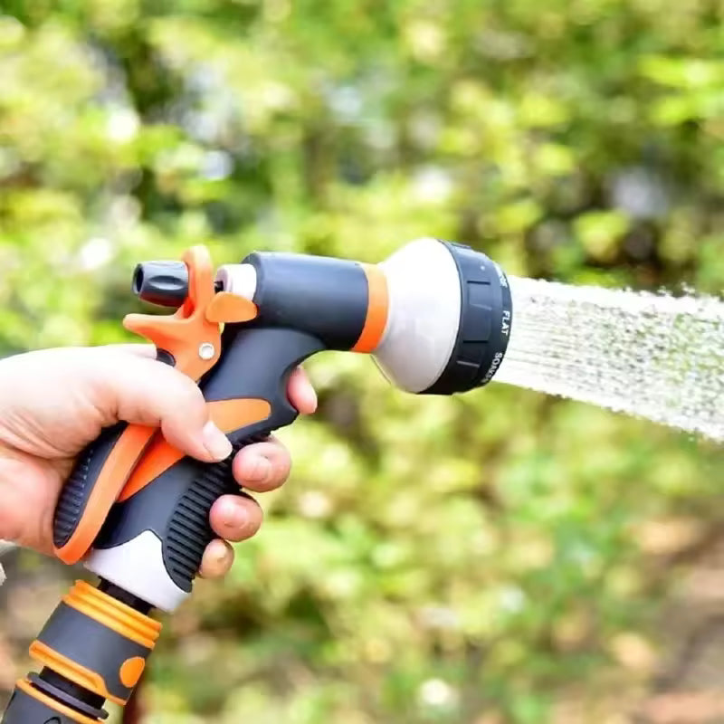 Hand holding a black and orange 8 pattern water gun spraying water outdoors with green background
