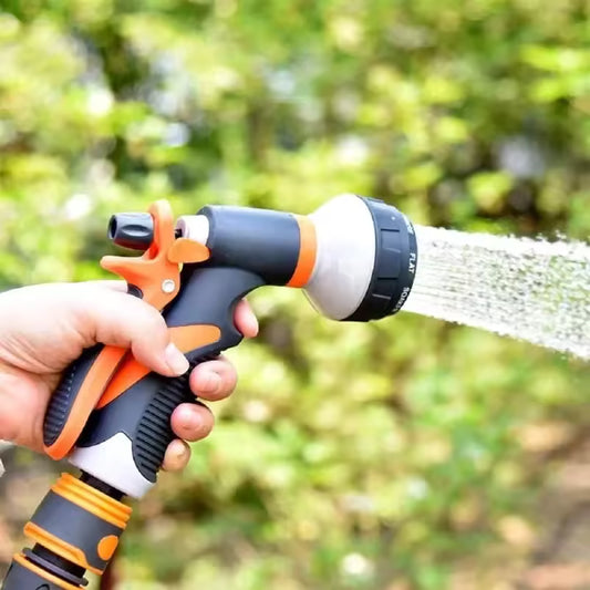 Hand holding a black and orange 8 pattern water gun spraying water outdoors with green background