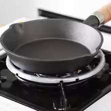 Gas stove stabilizer bracket supporting a black frying pan on a gas burner for cooking