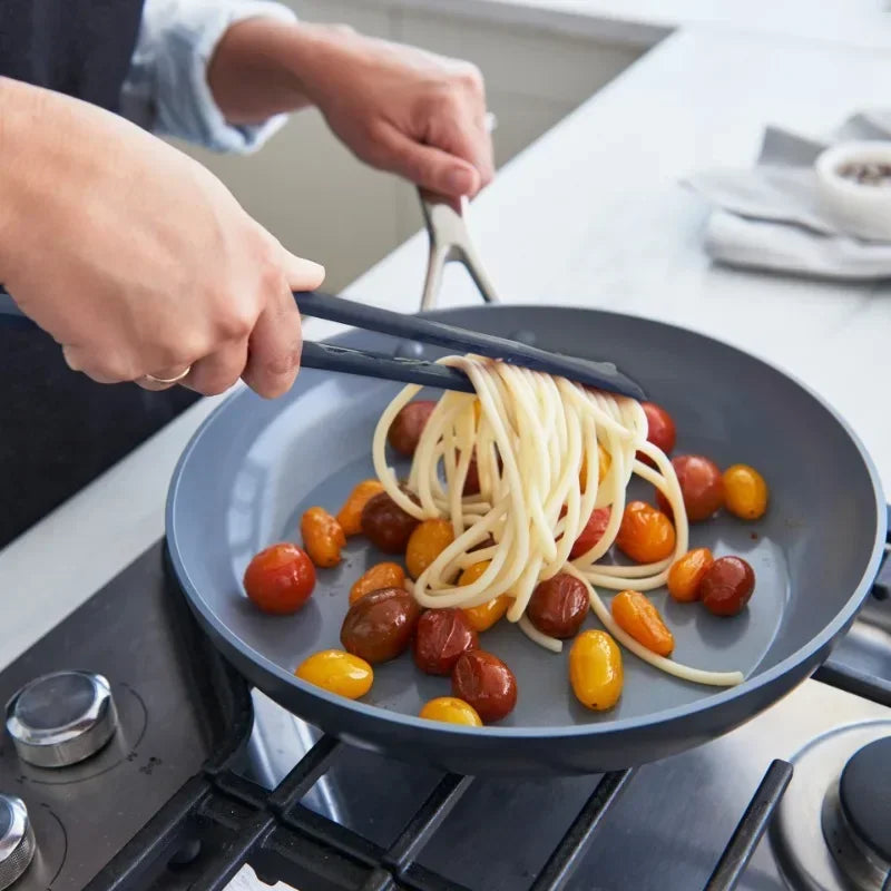 2 in 1 kitchen spatula lifting spaghetti and cherry tomatoes from a frying pan on stovetop