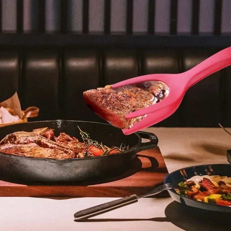 Pink 2 in 1 kitchen spatula lifting cooked steak from cast iron skillet on dining table