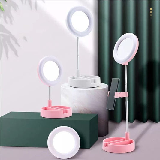 Pink and white foldable selfie stick with ring light and phone holder displayed on geometric platforms