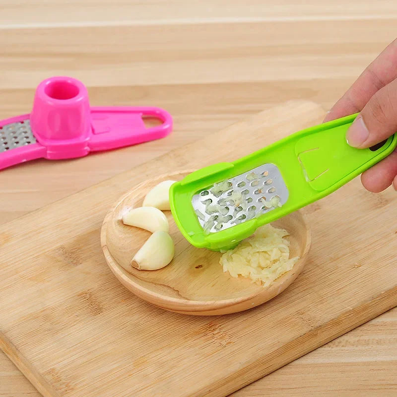 Clarify.pk green ginger garlic crusher tool crushing garlic on wooden plate with cloves nearby
