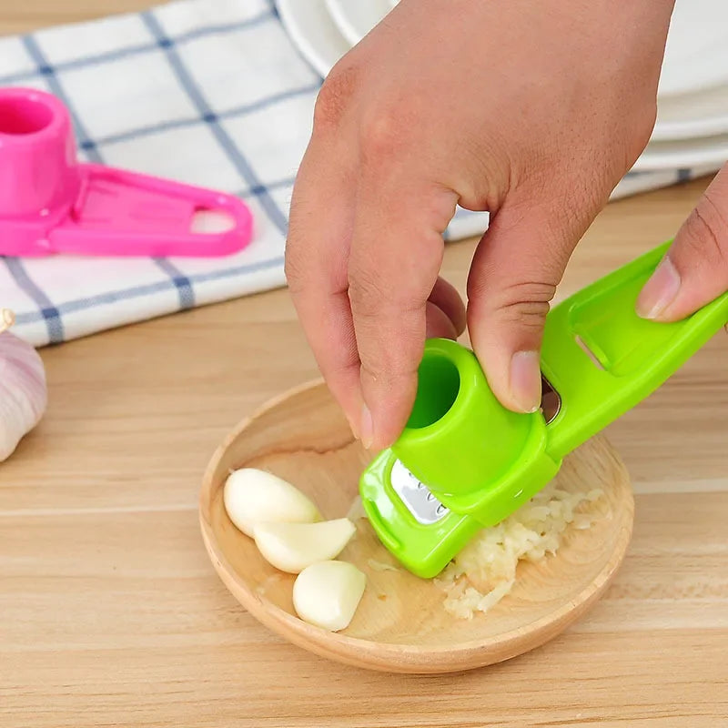 Green ginger garlic crusher tool pressing garlic cloves on wooden plate by Clarify.pk