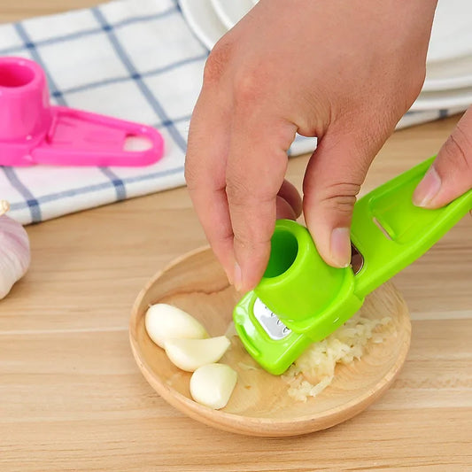 Green ginger garlic crusher tool pressing garlic cloves on wooden plate by Clarify.pk