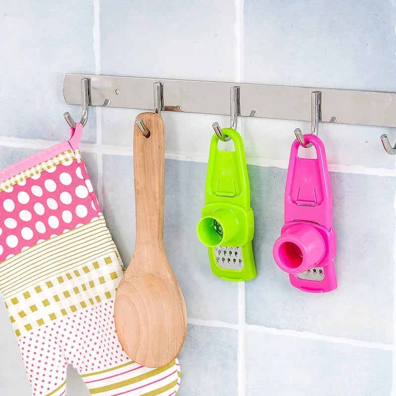 Clarify.pk colorful ginger garlic crusher tool hanging on kitchen wall with wooden spoon and oven mitt