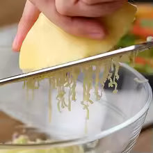 Mini stainless steel grater being used to grate cheese into a glass bowl
