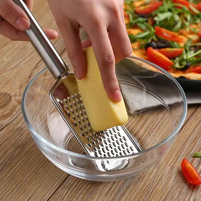 Clarify.pk mini stainless steel grater being used to grate cheese into a glass bowl on a wooden surface