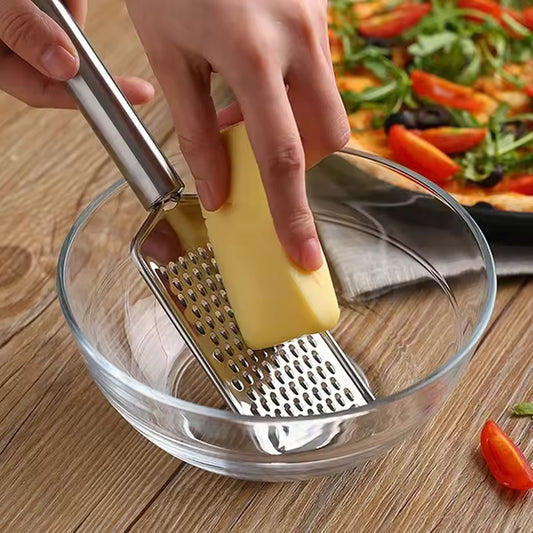 Clarify.pk mini stainless steel grater being used to grate cheese into a glass bowl on a wooden surface