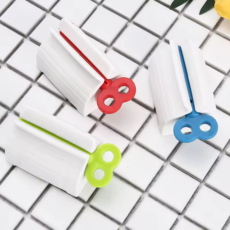 Set of three colorful toothpaste tube squeezers in red blue and green on white tiled surface
