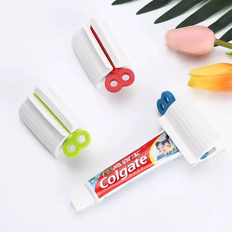 Three colorful toothpaste tube squeezer clips with a Colgate toothpaste tube on a white surface