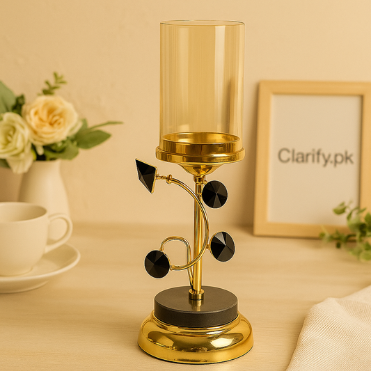 Geometric gold candle holder with black decorative accents and a glass cover on a wooden table