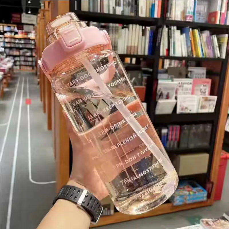 Pink 2 liter water bottle for girls with time markers and flip-top lid held in hand indoors