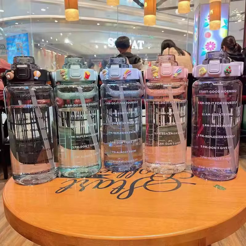 Clear 2 liter water bottle for girls with motivational time markings and colorful flip lids on table