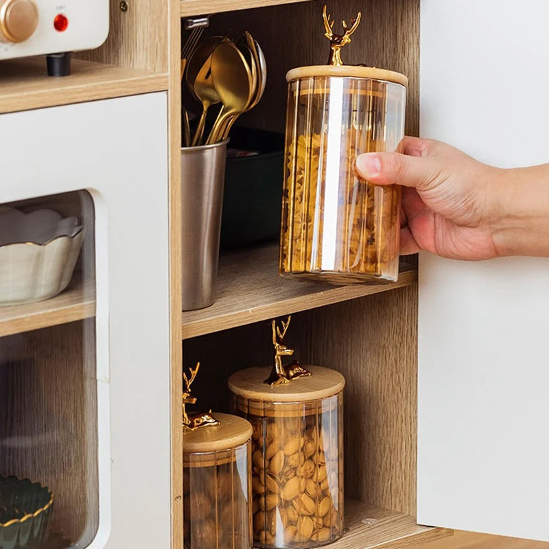 Hand placing a glass food jar with bamboo lid filled with nuts into a wooden kitchen cabinet