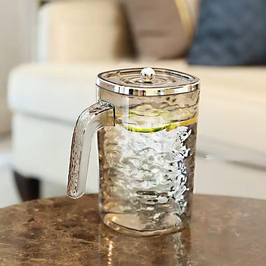 Clear glass juice pitcher with lid featuring a textured design and chrome handle on a marble table