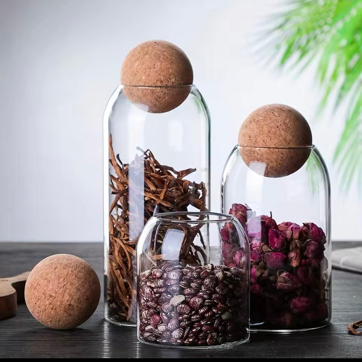 Set of glass storage jars with cork lids holding dried herbs and flowers on a wooden surface