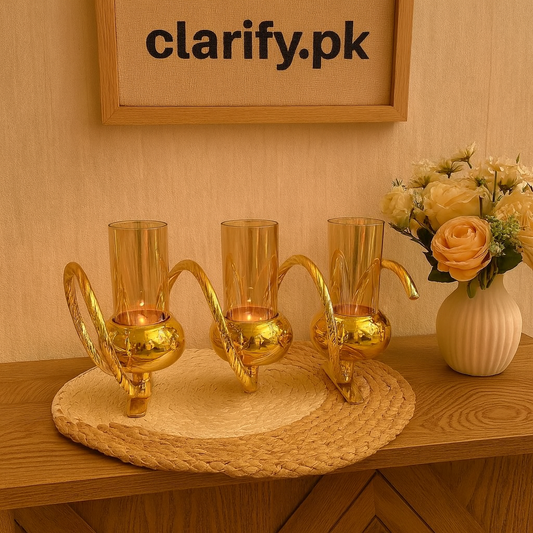 Elegant golden triple glass candle holder with curved handles displayed on a woven mat near decorative flowers