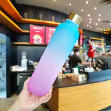 Gradient color outdoor water cup in blue to pink tones held in hand inside a cafe setting