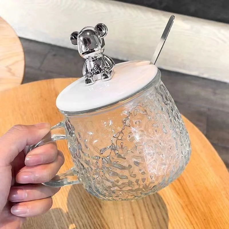 Hammered glass coffee cup with lid featuring a silver bear knob and a clear handle by Clarify.pk