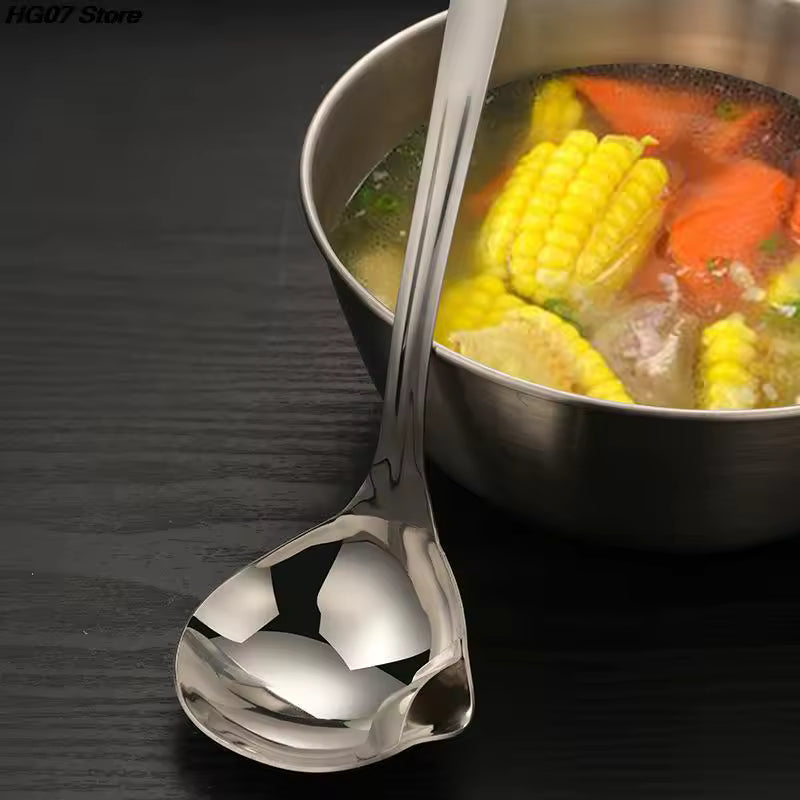 Stainless steel oil separator spoon next to a pot of vegetable soup with corn and carrots