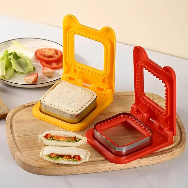 Yellow and red plastic sandwich cutter and sealer set on wooden board with sealed square sandwiches and tomato slices