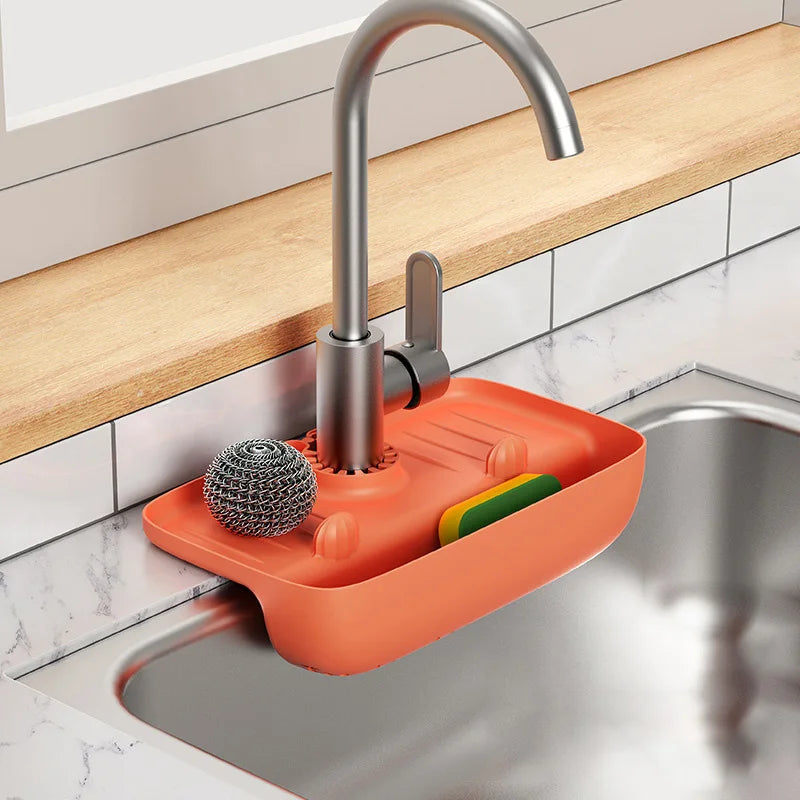 Orange silicone faucet mat with scrubber and sponges attached to kitchen sink faucet