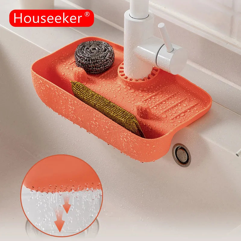 Orange silicone faucet mat by Clarify.pk installed under white faucet holding scrubber and corn