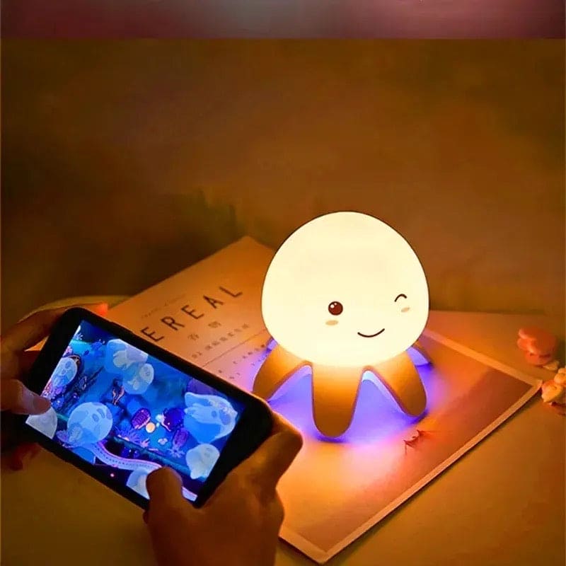 Cute smiling jellyfish night light glowing softly on a table with phone displaying jellyfish images