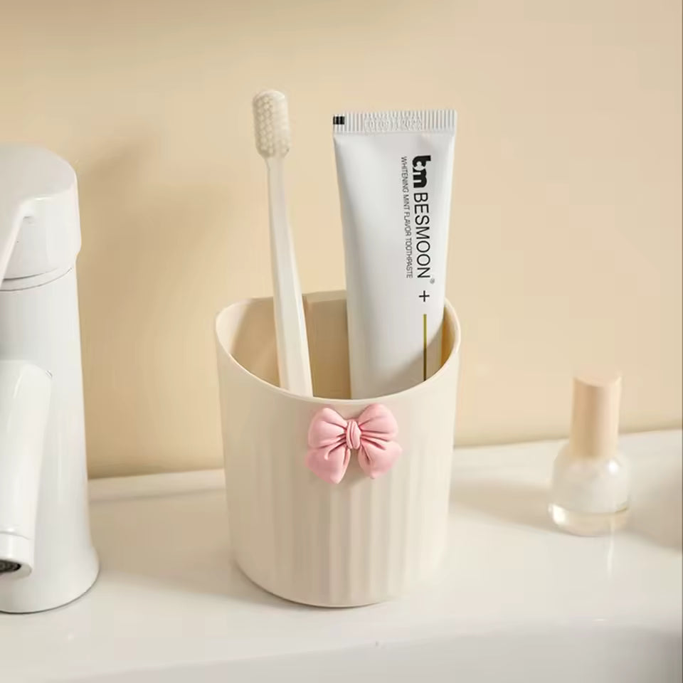 Cream colored kawaii pen holder for desk with pink bow holding toothbrush and tube on white surface