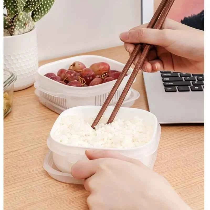 Hands using chopsticks in white kitchen food storage containers with rice and grapes on a desk
