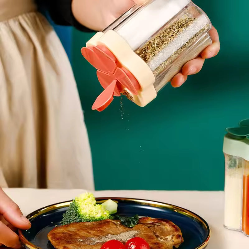 Hand holding kitchen seasoning container with lids sprinkling herbs over cooked meat and vegetables