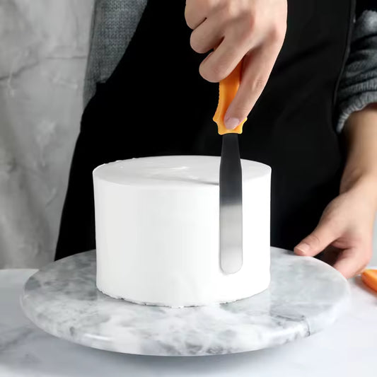 Person using cake spatula 3 piece set with orange handle to smooth white frosting on round cake