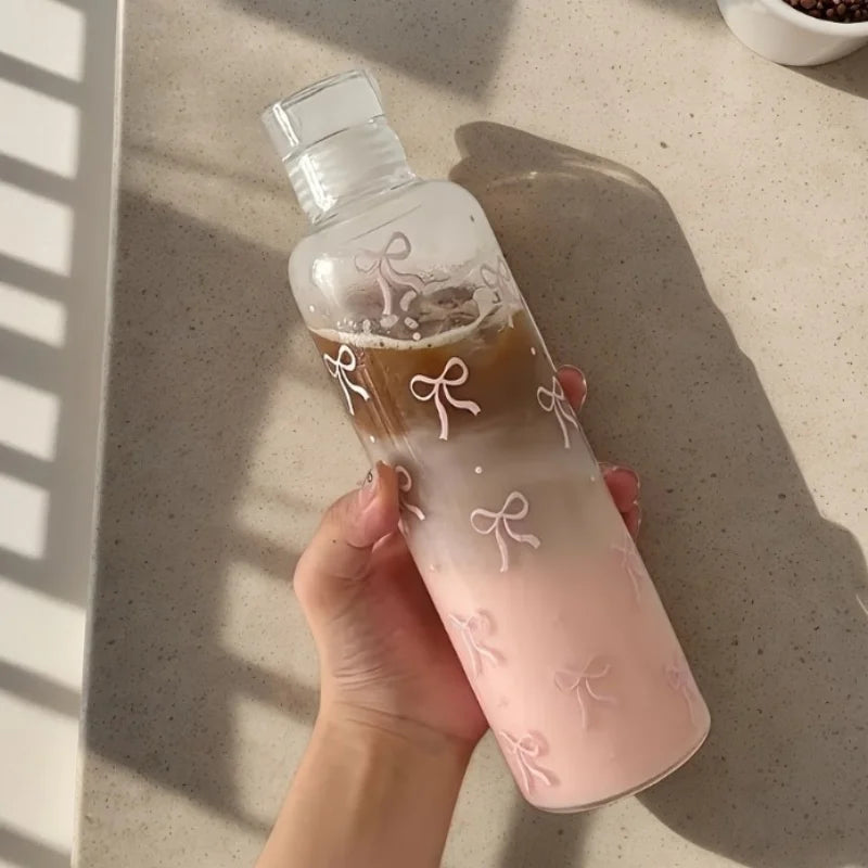 Hand holding a pink and brown leakproof sport water bottle with bow designs on a beige surface