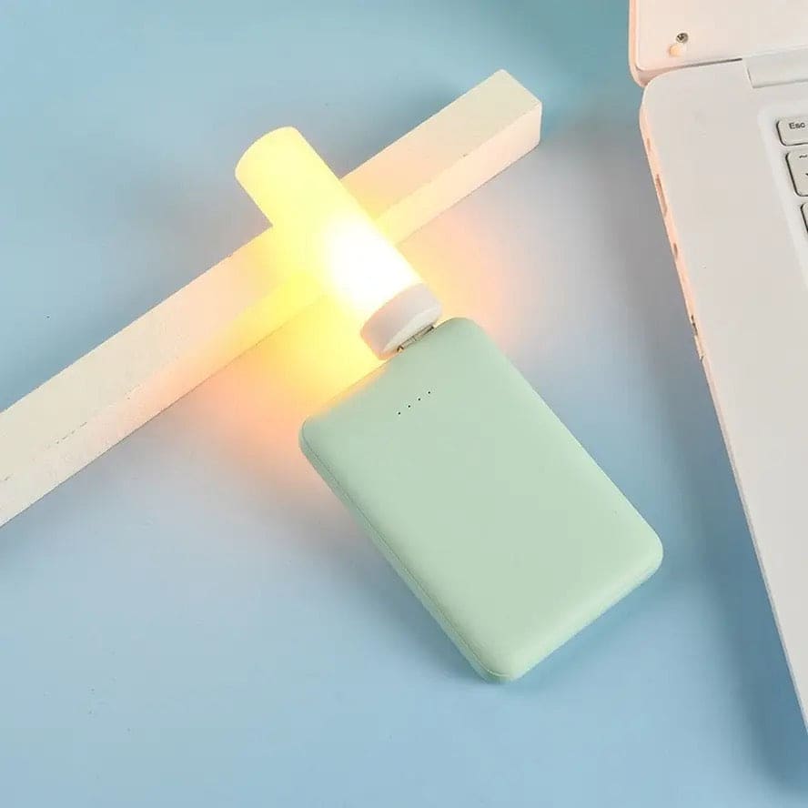 Compact LED flame effect night light plugged into a mint green portable charger beside a laptop