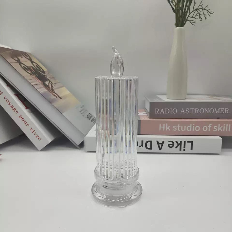 Clear LED flameless candle lamp with ribbed glass design on white surface near books and vase