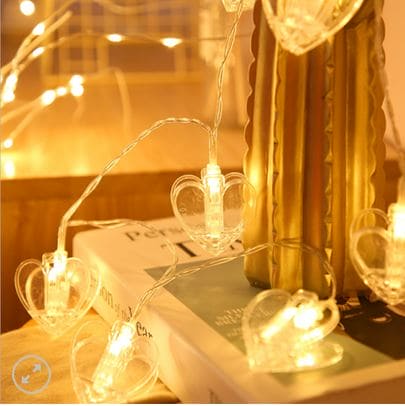Warm white LED photo clip string lights with transparent heart clips decorating a cozy indoor setting