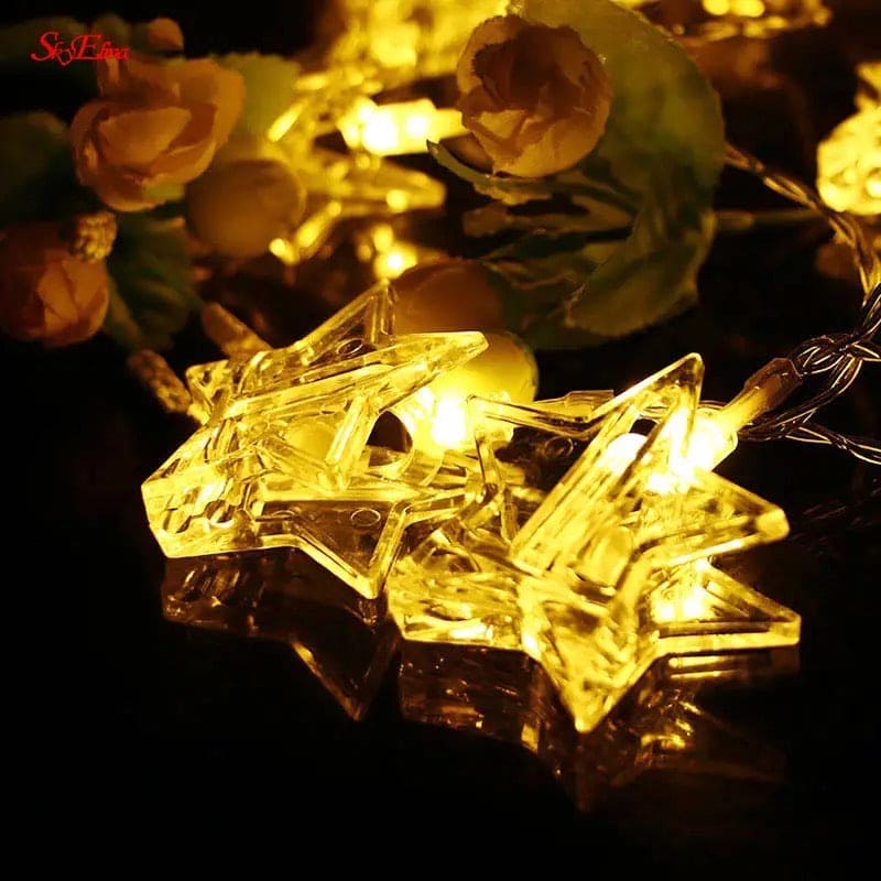 Star-shaped LED photo clip string lights glowing warmly with decorative flowers in the background