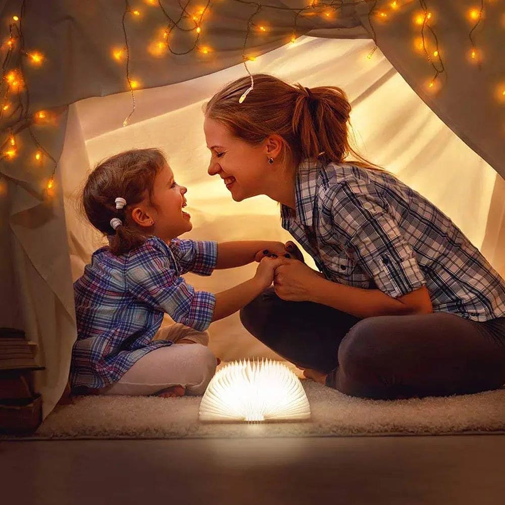 LED wooden book lamp glowing warmly between mother and daughter inside cozy tent with string lights