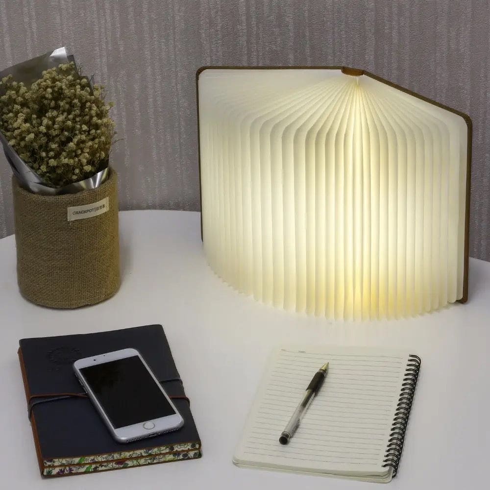 Clarify.pk LED wooden book lamp glowing on desk next to notebook phone and flower vase
