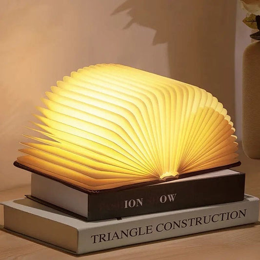 Open LED wooden book lamp glowing warmly on two stacked books on a wooden surface