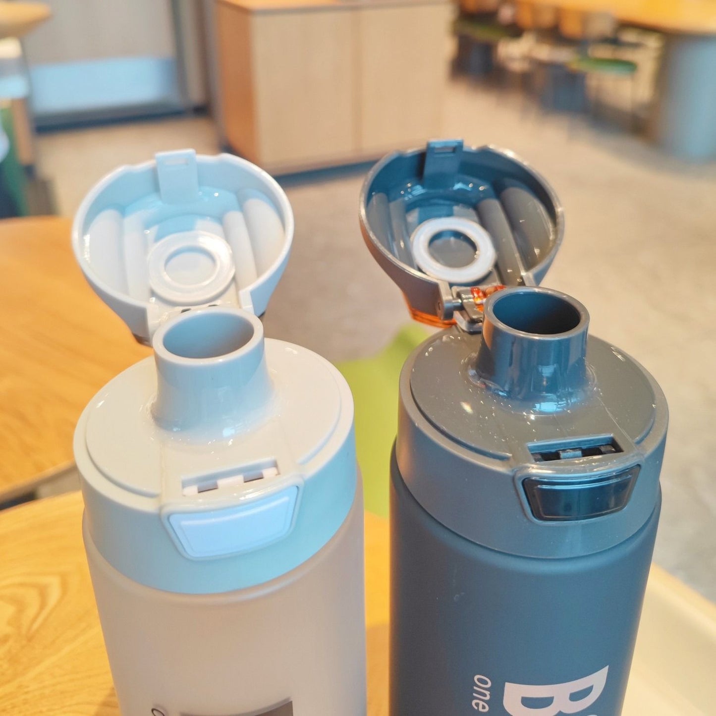 Two 1000ml sports water bottles with flip-top lids in gray and white on a wooden table