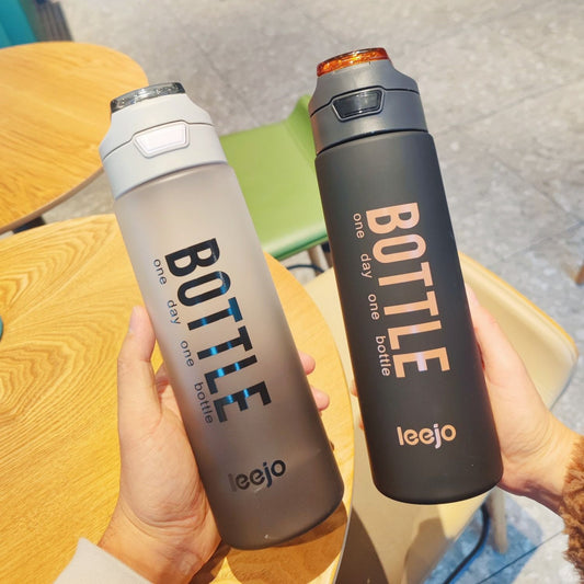 Two 1000ml sports water bottles in gray and black with flip caps held over wooden table