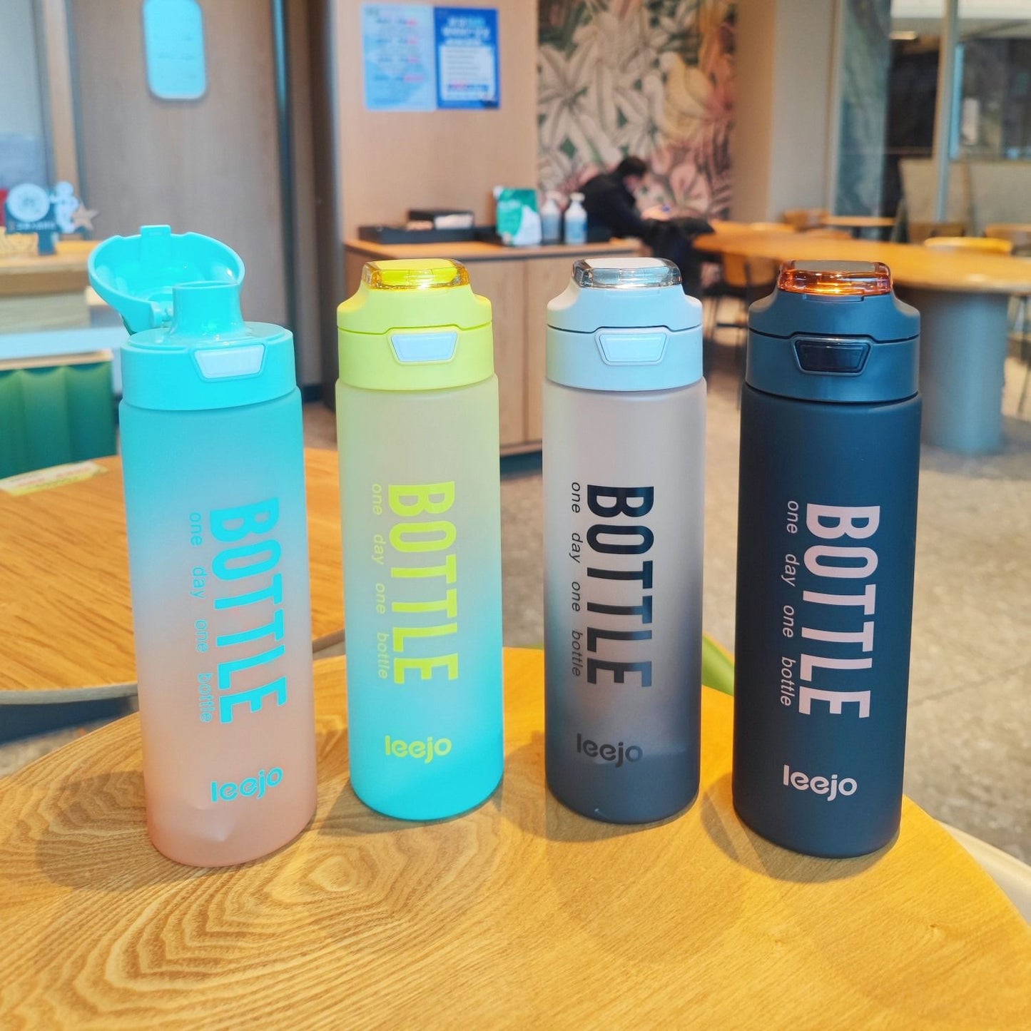 Set of four colorful 1000ml sports water bottle with flip-top lids and modern design placed on a wooden table