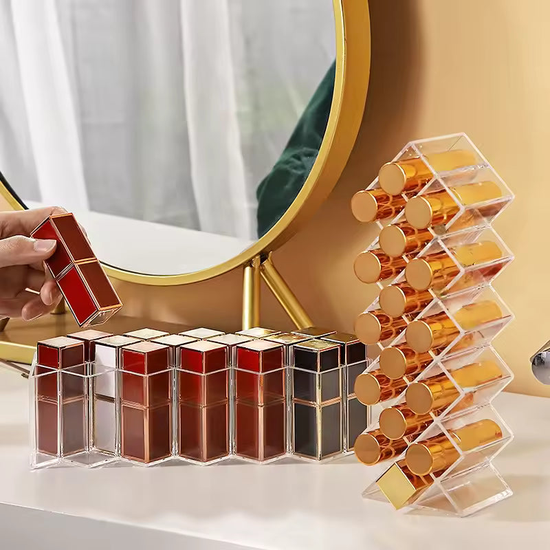Clear lipstick organizer with compartments holding gold-capped lipsticks on vanity next to round mirror